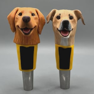 May include: Two dog-themed bottle stoppers. One is a golden retriever, the other a yellow lab. Both have smiling faces, yellow collars with black rectangles, and silver stems. The stoppers are likely made of resin or a similar material.