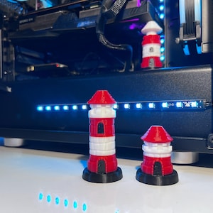 May include: Three lighthouse figurines in varying sizes, each featuring a red and white striped tower, a red conical roof, and a black circular base. The structures have small black rectangular openings at the base and mid-section, with a white gallery.