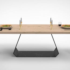 May include: A contemporary dining table with a light wood surface and a black geometric base. Two red chairs with woven seats are positioned either side. The table is set with plates of food, candles, and a wine glass.