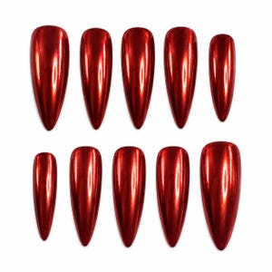 Könnte beinhalten: Ein Set aus zehn künstlichen Fingernägeln in einem leuchtenden, metallisch roten Finish. Jeder Nagel hat eine lange, spitz zulaufende Stiletto-Form mit einer glatten, reflektierenden Oberfläche, die das Licht einfängt und für einen Hochglanz-Look sorgt.