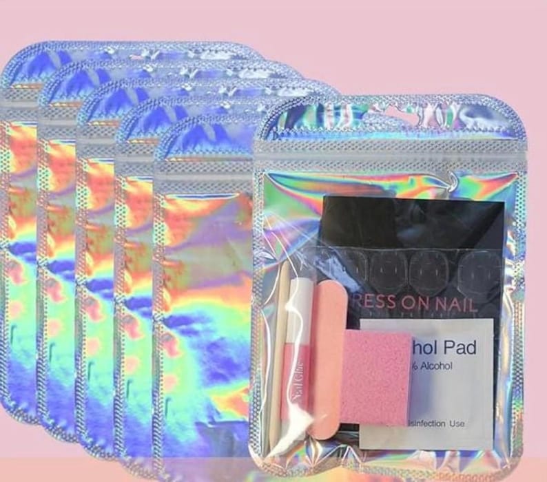 May include: Five holographic, iridescent resealable pouches containing nail application kits. Each kit includes a wooden cuticle stick, a small tube of nail glue, a pink nail file, a pink buffer block, and a white alcohol pad labeled Press on Nail.