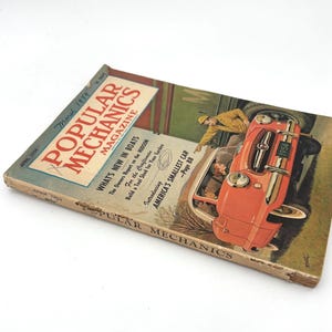 May include: Vintage March 1954 issue of Popular Mechanics magazine. The cover features an illustration of a red car with the text "America's Smallest Car." The magazine's title is in large red letters, with the issue date and price visible.
