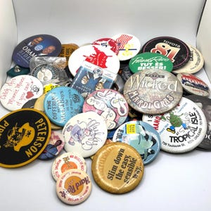 Peut inclure: Une collection de badges vintage avec divers motifs et textes. Les badges présentent des personnalités politiques, des logos d'événements et des slogans publicitaires. Les couleurs incluent le noir, le blanc, le jaune, le bleu et le rouge. Certains badges ont du texte comme "Wicked Mardi Gras".