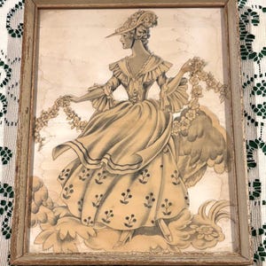 Puede incluir: Impresión enmarcada vintage de una mujer con vestido y sombrero de época, sosteniendo una guirnalda floral. La obra de arte está en tonos sepia, con una representación detallada del vestido y los detalles florales. El marco es de color marrón claro desgastado.