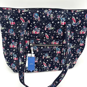 Puede incluir: Bolso tote acolchado azul marino con un estampado caprichoso de pájaros y flores. El bolso tiene una cremallera en la parte superior, un bolsillo exterior y dos asas. El estampado incluye pájaros en rojo, blanco y azul, con detalles florales blancos.
