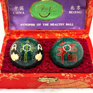 May include: A pair of green and black healthy balls with panda and Chinese character designs, presented in a red box with gold accents. The box contains text in Chinese and English, including "Synopsis of the Healthy Ball."