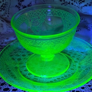 May include: A set of two vintage uranium glass dishes in a bright green color. The dishes have a footed bowl and a matching plate with a decorative pattern.