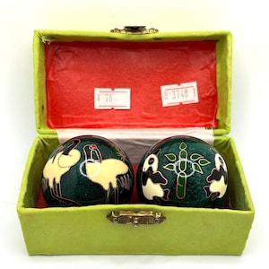May include: Two decorative Chinese health balls in a lime green box. The balls are dark green with gold and white crane and panda designs. The box has a red interior and a gold clasp.