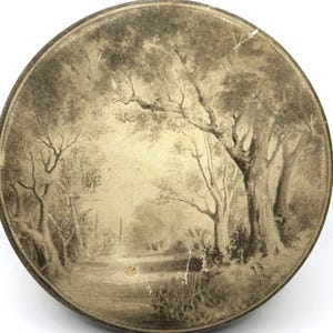 May include: Round, sepia-toned decorative piece featuring a detailed landscape scene. The artwork depicts a path winding through a forest with tall trees and foliage. The piece has a dark brown border and a slightly distressed appearance.