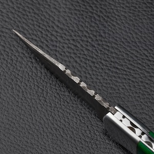 Close-up of custom Damascus steel folding knife spine showing detailed file work and blade texture, 
highlighting craftsmanship and precision forging—perfect for collectors, EDC, and handmade knife enthusiasts.