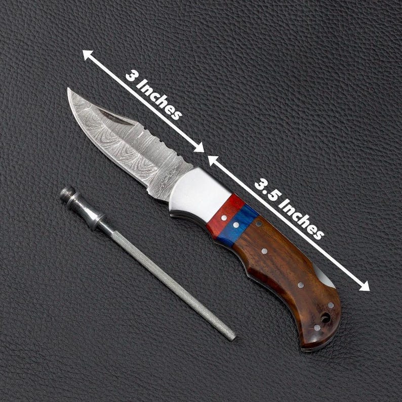 May include: A folding knife with a patterned Damascus steel blade, a silver bolster, and a handle featuring red, blue, and brown wood segments. The blade measures 3 inches and the handle measures 3.5 inches. A thin metal sharpening rod is included.