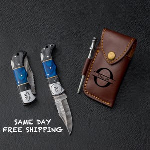 May include: Two personalized pocket knives with blue and black handles, a leather sheath with a monogram, and a small tool. The knives have the initials "MK" and "OJ" engraved on them. The sheath has the initial "O" and the name "Oswalt" engraved on it.  SAME DAY FREE SHIPPING.