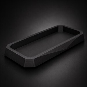 Könnte beinhalten: Eine schwarze rechteckige Ablage mit geometrischem Design. Die Ablage hat einen erhöhten Rand und einen flachen Boden. Die Seiten der Ablage sind abgewinkelt und die Ecken leicht abgerundet. Die Ablage ist aus dunklem Material.