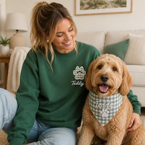 May include: A dark green crewneck sweatshirt featuring an embroidered grey and white plaid paw print with the name Teddy underneath. A matching grey and white plaid dog bandana is worn by a golden-colored dog, also embroidered with the name Teddy.