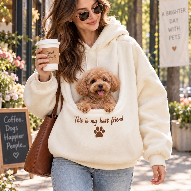 May include: A cream-colored fleece hoodie featuring a large front pouch containing a small brown poodle. The hoodie has the text "This is my best friend" embroidered in brown above a brown paw print graphic on the front pocket area.