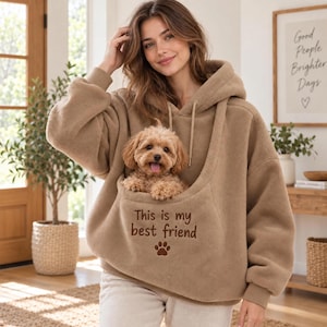 May include: A tan fleece hoodie featuring a large front pouch containing a small light brown puppy. The hoodie has long sleeves, a hood with drawstrings, and the embroidered text "This is my best friend" above a small brown paw print icon.
