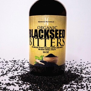 Puede incluir: Una botella de vidrio de amargos de semillas negras org&aacute;nicos con una etiqueta dorada que dice "GENNAIO NATURALS ORGANIC BLACKSEED BITTERS AID DIGESTION, DETOXIFY THE BODY, SUPPORT LIVER HEALTH AND BOOST OVERALL VITALITY. 16 OZ". Semillas de s&eacute;samo negras est&aacute;n esparcidas alrededor de la botella.