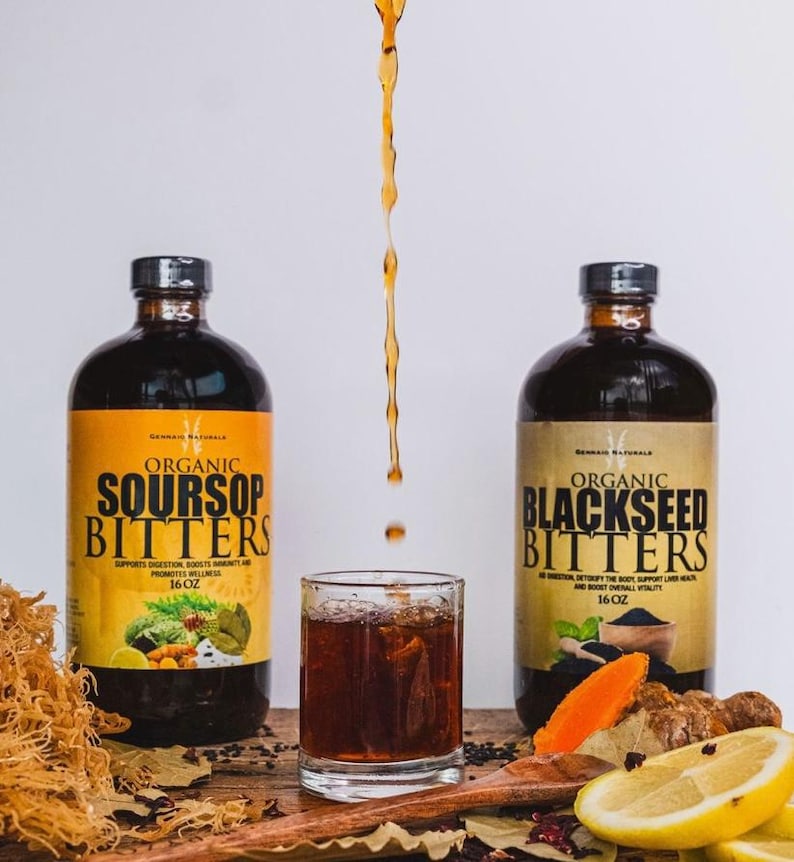 Puede incluir: Dos botellas de 473 ml de amargos org&aacute;nicos, una etiquetada como "Soursop Bitters" y la otra como "Blackseed Bitters". Las botellas son de vidrio marr&oacute;n con una etiqueta negra y texto blanco. Las botellas est&aacute;n sobre una superficie de madera con un vaso de l&iacute;quido oscuro y varios ingredientes como rodajas de lim&oacute;n, c&uacute;rcuma y semillas negras.