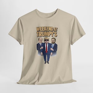 May include: A beige t-shirt featuring a cartoon illustration. The graphic depicts three men, one wearing sunglasses and a red tie, with the text "WEEKEND AT TRUMPY'S" in an orange and yellow font.