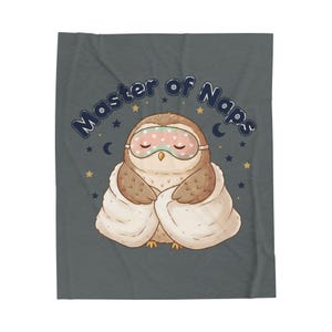 May include: A gray blanket featuring a cartoon owl wearing a sleep mask and wrapped in a blanket. The text "Master of Naps" is arched above the owl, with stars and crescent moons scattered around the design.