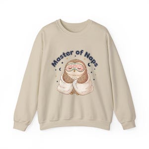 May include: Beige sweatshirt with a graphic of a cartoon owl wearing a sleep mask and wrapped in a blanket. The text "Master of Naps" is arched above the owl in blue letters, with stars and crescent moons.