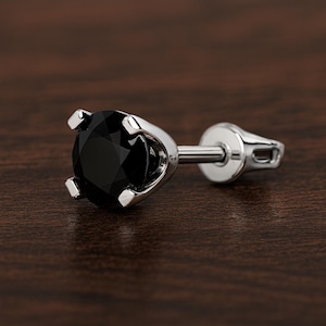 Peut inclure: Une boucle d'oreille à tige unique avec une pierre précieuse noire ronde et facettée, montée sur un sertissage à griffes en métal argenté. Le bijou comprend un fermoir plat et circulaire, offrant une finition métallique et un design épuré.