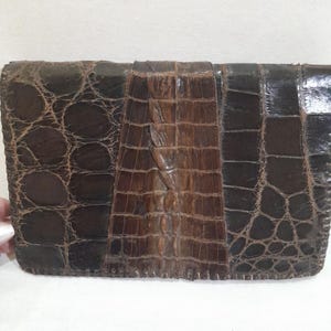 May include: A brown leather clutch purse with a crocodile skin pattern. The purse has a flap closure and a stitched edge.