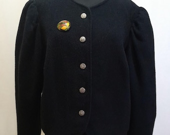 May include: A black wool jacket with a round neckline and button fastening. The jacket has puffed sleeves and silver buttons. A small, round, colourful pin is attached to the left side of the jacket.