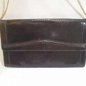 May include: A dark brown snakeskin clutch purse with a gold chain strap.