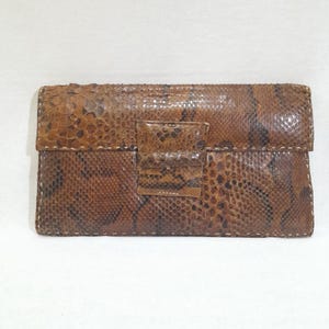 May include: A brown snakeskin clutch bag with a flap closure and a stitched design.