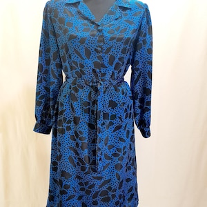 Peut inclure: Une robe à manches longues avec un imprimé de feuilles bleu vif et noir. Le vêtement présente un col, une fermeture boutonnée sur toute la longueur à l'avant et une ceinture à nouer assortie à la taille pour une silhouette cintrée.