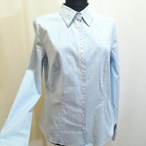 May include: A long-sleeved button-down shirt featuring a light blue and white gingham check pattern. The shirt has a pointed collar, a full-length front button placket with small white buttons, and long sleeves with cuffs, displayed on a mannequin.