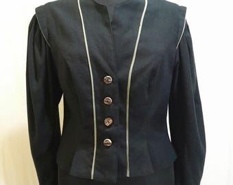 May include: A black jacket with a mandarin collar and long sleeves. The jacket has four decorative buttons down the front and is trimmed with light-coloured piping. The jacket is displayed on a mannequin.