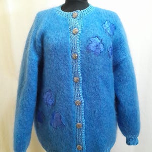 Peut inclure: Un cardigan bleu en fourrure avec des feuilles bleues brodées et des boutons argentés.