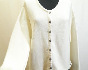 May include: A cream-coloured cardigan sweater with a V-neck and long sleeves. The sweater has a ribbed knit texture and is fastened with seven round, silver-toned buttons. The hemline and cuffs have a subtle, scalloped edge.