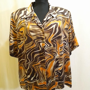 Może przedstawiać: Koszula zapinana na guziki z krótkim rękawem z wirującym wzorem w odcieniach brązu, beżu i pomarańczy. Koszula jest prezentowana na czarnym manekinie. Tkanina ma jedwabisty połysk.