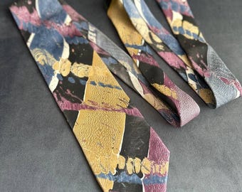 Può includere: Una cravatta con motivo a stampa con un design astratto in nero, oro, blu e viola. La cravatta è realizzata in tessuto strutturato.
