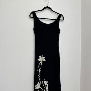 Könnte beinhalten: Ein schwarzes, ärmelloses Maxikleid mit einem weißen Blumenmuster auf der unteren Hälfte.