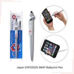 Può includere: Penna a sfera argento a 3 vie con punta stilo nera e la scritta "EXPO 2025". La penna funge anche da supporto per smartphone. La penna è mostrata nella sua confezione e in uso.