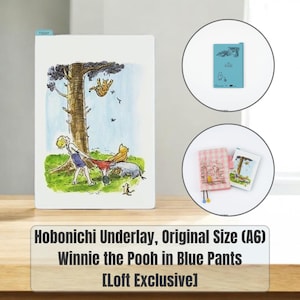 May include: A rectangular Hobonichi A6 underlay featuring a Winnie the Pooh illustration of characters near a tree. The set includes a blue plastic sheet with character outlines and a small notebook with a pink checkered cover and a Pooh graphic.