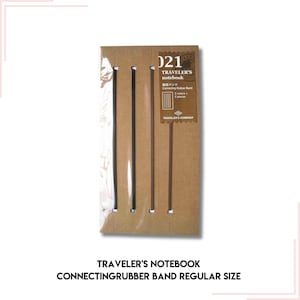 Può includere: Un taccuino Traveler's Notebook marrone con un elastico di collegamento. Il taccuino ha un timbro di data 2021 e il testo "Connecting Rubber Band" in giapponese.