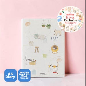 May include: A white A6 diary for 2027 featuring illustrations of cats, hanging plants, and furniture. The cover includes the text 2027 Datebook and Midori. A circular sticker sheet overlay displays the text Includes Eiya Exclusive Stickers.