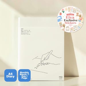 May include: A white A5 MD Notebook Diary for 2027 featuring a line drawing of a hand writing the year. The cover includes text in Japanese and English. A circular sticker sheet labeled Includes Eiya Exclusive Stickers is attached to the top right.