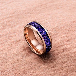 Könnte beinhalten: Roségoldener Ring mit einem Band aus tiefvioletten Steinen. Der Ring hat eine polierte Oberfläche und ein modernes Design. Die violetten Steine sind in einem Kanal gesetzt, was einen auffälligen Kontrast zum Roségold erzeugt.