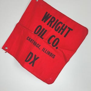 May include: A red cloth flag with black text reading "WRIGHT OIL CO." and "CARTHAGE, ILLINOIS" and "DX." The flag has metal grommets in the corners. The flag is folded and slightly wrinkled.