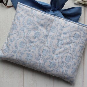 May include: A white fabric clutch with a blue floral pattern and a blue ribbon closure.