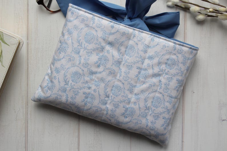 May include: A white fabric clutch with a blue floral pattern and a blue ribbon closure.
