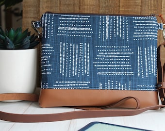 Op de afbeelding: Een blauwe en witte crossbody tas met een bruin leren bandje en afwerking.