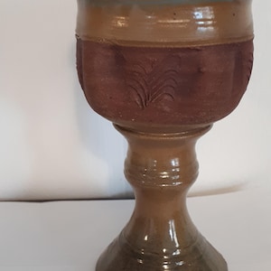 Op de afbeelding: Een bruine keramische beker met een groene voet en een bruin en rood lichaam met een gesneden ontwerp.