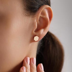 May include: A pair of gold hexagon stud earrings. The earrings are small and simple, and they would make a great everyday accessory.